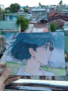 a person holding up a drawing of a girl with blue hair in front of some buildings