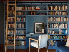 a living room filled with lots of books on top of blue bookcases next to a ladder