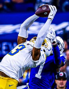 two football players colliding over each other in the air with their hands up