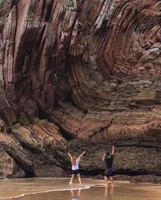 two people standing on the beach with their arms in the air