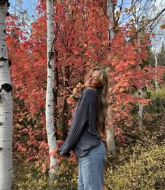 a woman standing in front of some trees with red leaves on it's branches