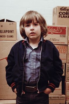 a young boy standing in front of boxes with his hands on his hips and looking at the camera