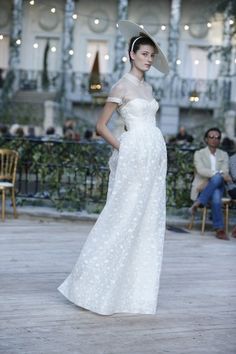 a woman in a white dress and hat walks down the runway at a fashion show