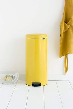 a yellow trash can sitting on the floor next to a basket and coat hanger