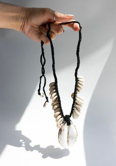 a hand holding a necklace with shells on it's string and black beaded cord