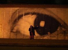 a woman standing in front of a wall with an image of a person's eye on it