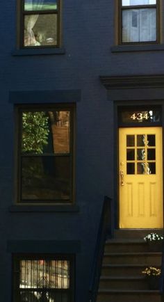 a yellow door is on the side of a blue building with black steps and windows