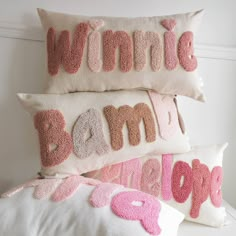 three pillows with pink and white letters on them, one is made out of yarn