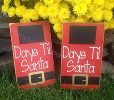 two wooden signs that say days til santa and day til santa on them in front of some yellow flowers