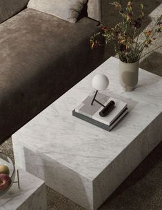 a white marble coffee table with a book and vase on it next to a couch