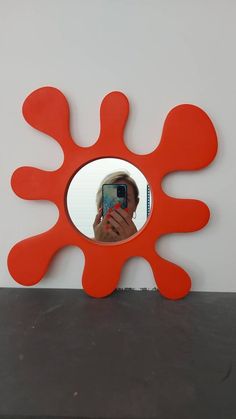 a person taking a photo in a mirror with an orange flower shaped object behind them