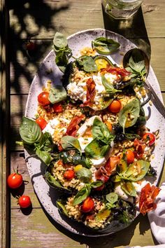 a white plate topped with lots of food on top of a wooden table next to tomatoes