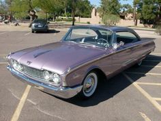 an old purple car parked in a parking lot