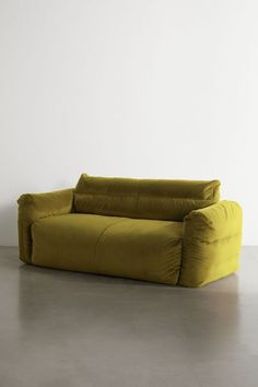 a yellow couch sitting on top of a cement floor next to a white wall in an empty room