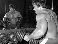 two men working out with dumbbells in a gym, one looking at the other