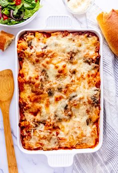 a casserole dish with meat, cheese and vegetables next to bread on a table