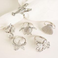 five rings with seashells on them sitting on a white surface next to a napkin