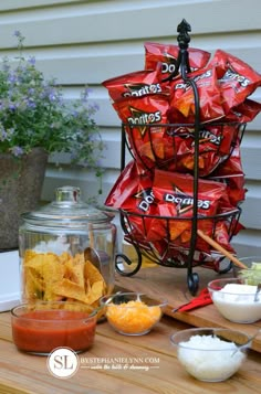 a table with chips and dips on it next to a glass jar filled with sauce