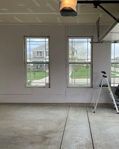 an empty room with three windows and a ladder in the foreground, next to two large windows