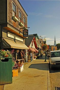 a truck parked on the side of a road next to buildings and shops with people walking by