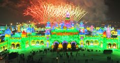 fireworks are lit up in the sky above a castle with lights on it and people walking around