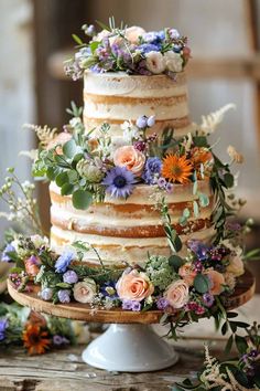 a wedding cake with flowers and greenery on the top is sitting on a wooden table