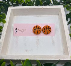 two orange basketballs are sitting in a white tray next to some green leaves and a pink sticker