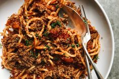 a white plate topped with spaghetti and meat sauce next to a fork on top of a table