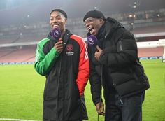 two men standing next to each other on a field with microphones in their hands