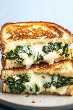 two grilled cheese and spinach sandwiches stacked on top of each other with melted cheese