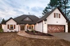 a white brick house with brown shutters on the front and garage doors open to let in light