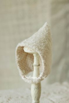 a small white hat is on top of a wooden stand with a cloth covering it