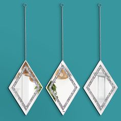 three diamond shaped mirrors hanging from chains on a blue wall, one with a plant in it