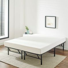 a bed frame with no sheets on it in a white room next to a window