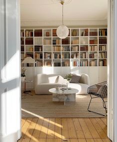 a living room filled with furniture and bookshelves next to a doorway that leads to a sitting area