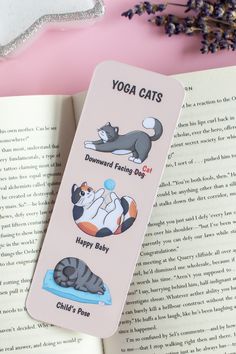 a bookmark with cats on it sitting next to an open book and lavender flowers