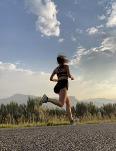 a woman is running down the road with her hair blowing in the wind while wearing black shorts