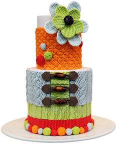 a multi - tiered cake decorated with flowers and knitted fabric, on a plate