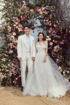 a man and woman standing in front of a floral arch