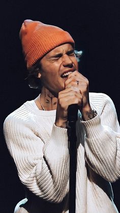 a man with an orange hat on holding a microphone in front of his face and wearing a white sweater