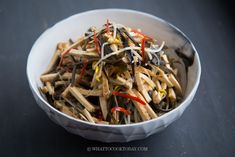 a white bowl filled with lots of food on top of a black table next to a fork