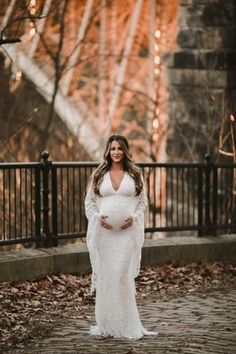 a pregnant woman wearing a white gown and holding her belly while standing in front of a fence