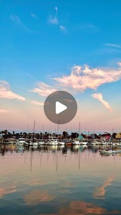 boats are docked in the water at sunset with clouds and blue sky above them, as seen from across the bay