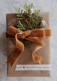 a present wrapped in brown paper with a ribbon tied around it and some greenery on top