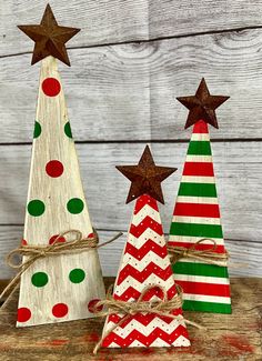 three small wooden christmas trees on top of a wooden table with red, green and white stripes