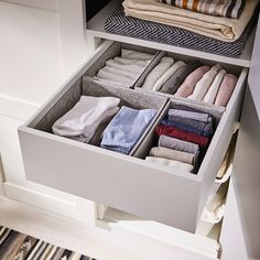 an organized drawer with folded towels and folded blankets in the bottom section, on top of a white cabinet