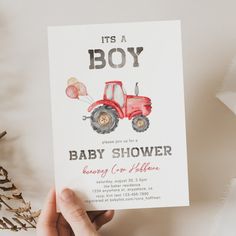 a hand holding up a baby shower card with a tractor on it and balloons in the air