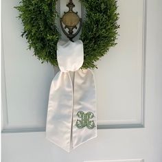 a green wreath on the front door with a monogrammed tie hanging from it