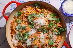 a red pan filled with pasta and parmesan cheese on top of a table