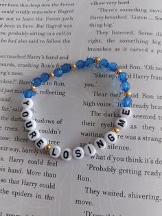 a bracelet with words written in white and blue beads on top of an open book